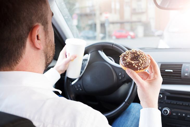 Man having breakfast and driving seated in car